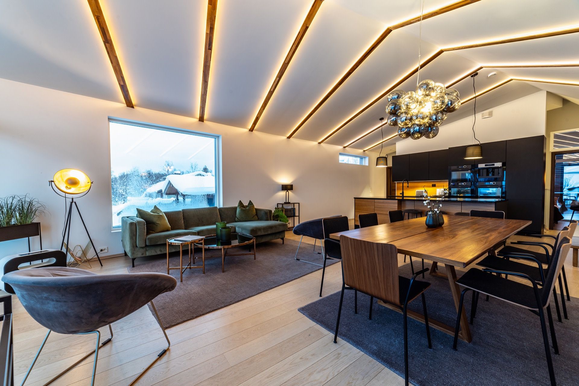Open-plan living and dining room under strips of light, snow outside the window